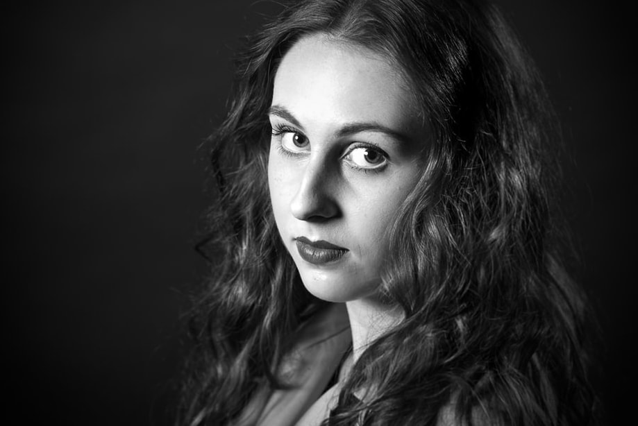Krachtig zwart-wit portret van een jonge, opgemaakte vrouw, genomen in een studio met zwarte achtergrond.